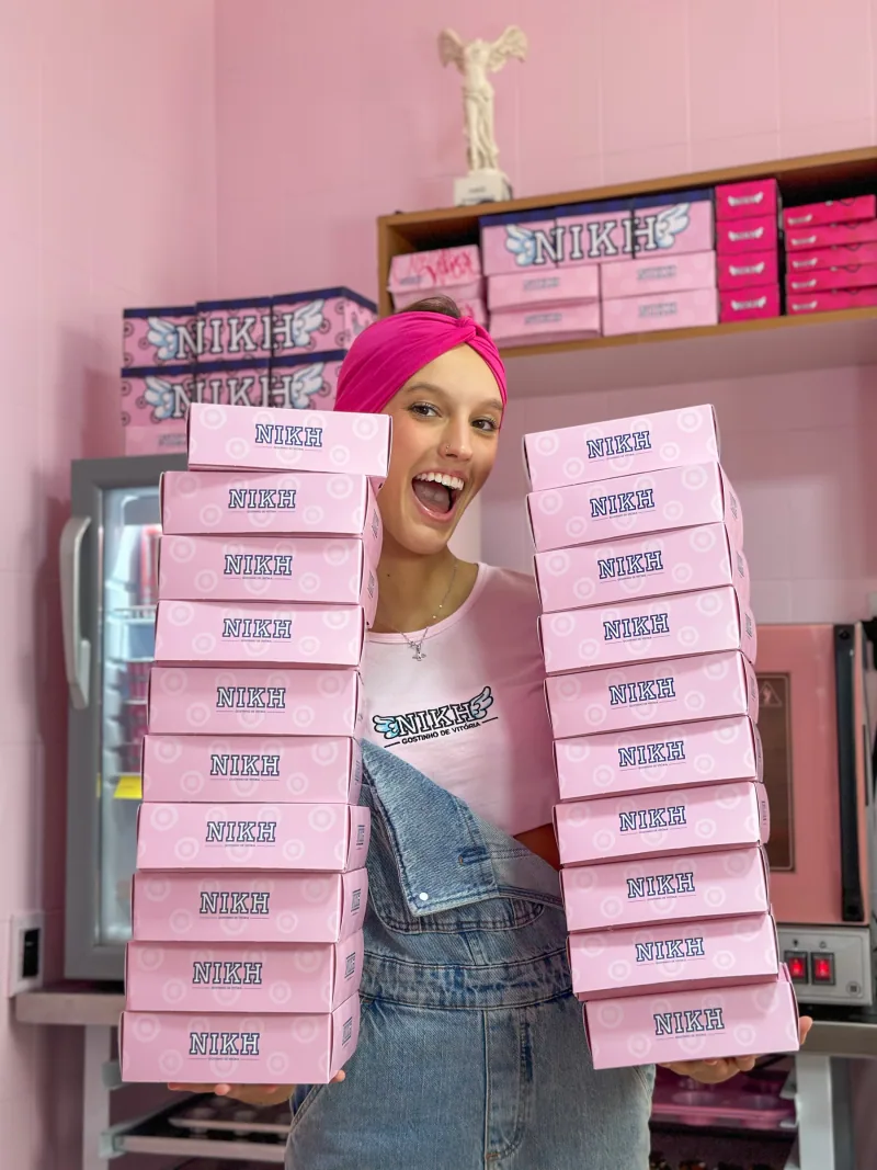 Nikh segurando duas pilhas de caixas rosa da Nikh Sweet na cozinha